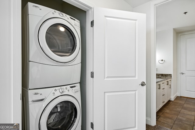 laundry area with dark tile patterned flooring and stacked washer / dryer