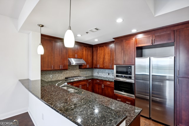 kitchen with hanging light fixtures, decorative backsplash, kitchen peninsula, stainless steel appliances, and hardwood / wood-style floors