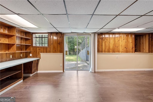 empty room with hardwood / wood-style flooring, a drop ceiling, and wood walls