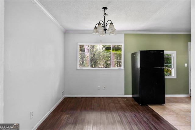 unfurnished dining area featuring wood-type flooring, an inviting chandelier, ornamental molding, and a textured ceiling