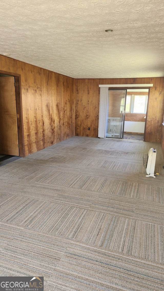 carpeted empty room with a textured ceiling and wood walls