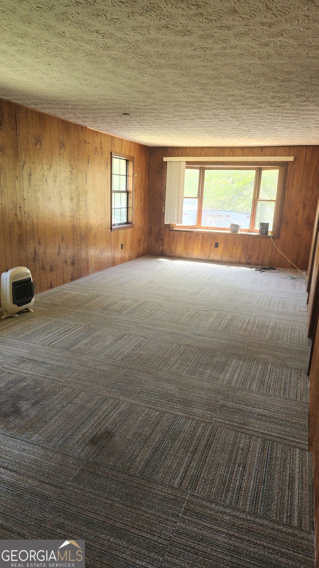 carpeted spare room featuring a textured ceiling, wooden walls, and heating unit