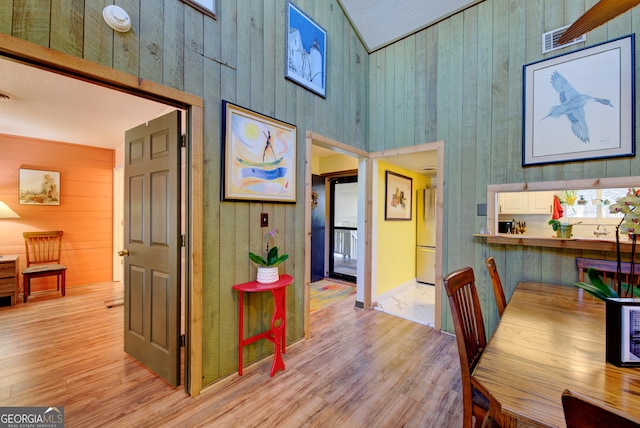 dining area with wood walls, a towering ceiling, and light hardwood / wood-style flooring