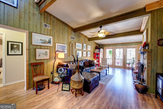 living room with light wood-type flooring, wood walls, beam ceiling, and ceiling fan