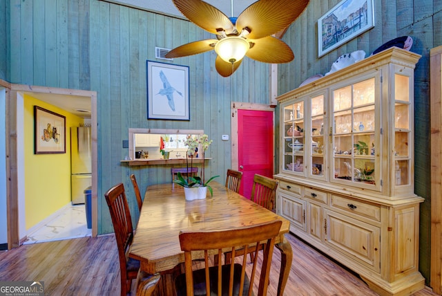 dining room featuring light wood-type flooring, ceiling fan, and wooden walls