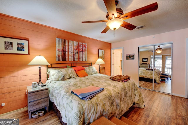 bedroom featuring ceiling fan, a closet, light wood-type flooring, and wood walls