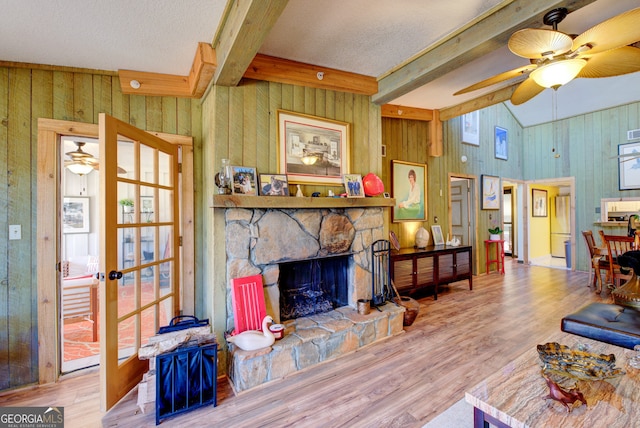 living room with ceiling fan, a stone fireplace, hardwood / wood-style flooring, and wooden walls