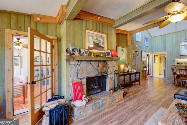 living room with wood walls, ceiling fan, hardwood / wood-style floors, and a stone fireplace