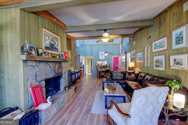 living room with a stone fireplace, ceiling fan, hardwood / wood-style flooring, vaulted ceiling with beams, and wooden walls