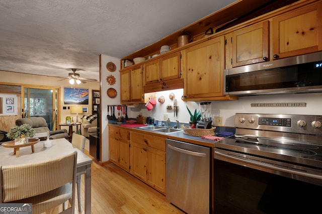 kitchen with appliances with stainless steel finishes, a textured ceiling, ceiling fan, light hardwood / wood-style flooring, and sink