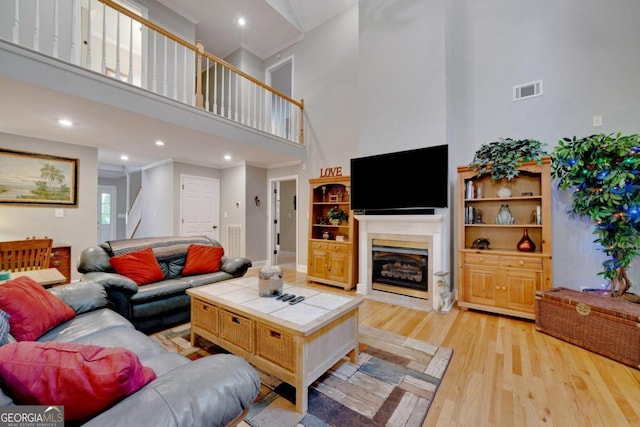 living room featuring built in shelves, light hardwood / wood-style floors, a premium fireplace, and a high ceiling