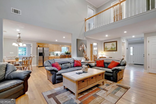 living room with a high ceiling, ornamental molding, light hardwood / wood-style flooring, and plenty of natural light