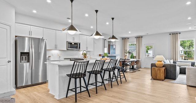 kitchen featuring a center island with sink, decorative light fixtures, stainless steel appliances, and plenty of natural light