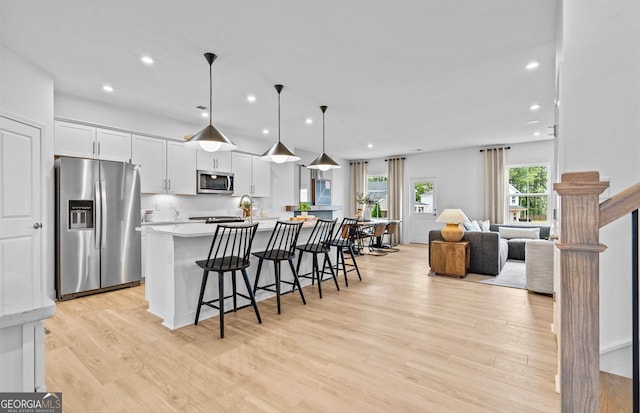 kitchen with hanging light fixtures, appliances with stainless steel finishes, white cabinetry, a kitchen bar, and light wood-type flooring