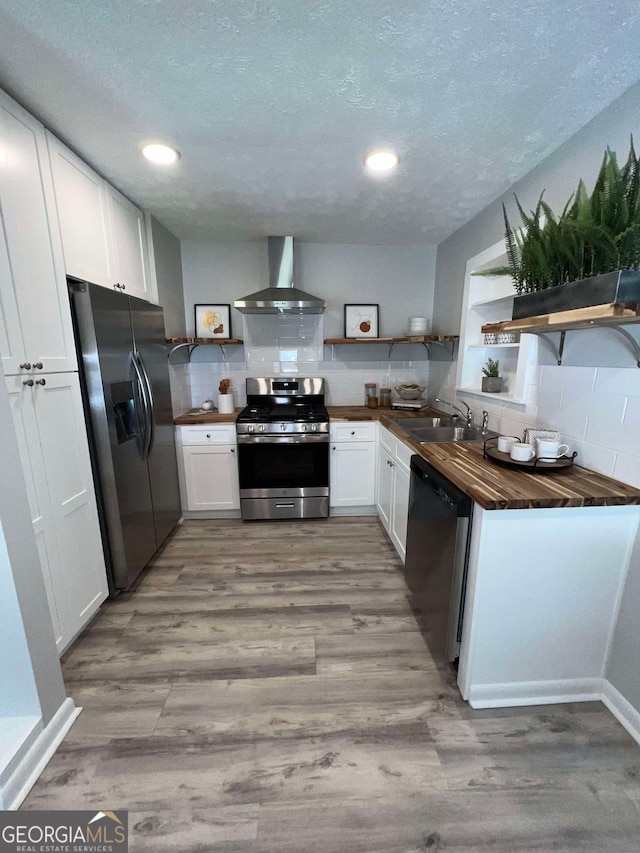 kitchen featuring appliances with stainless steel finishes, sink, wall chimney range hood, and white cabinetry