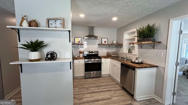 kitchen with white cabinets, sink, a textured ceiling, wall chimney range hood, and appliances with stainless steel finishes