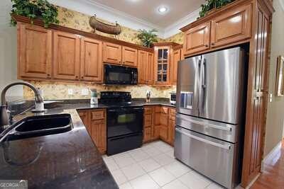 kitchen featuring light tile patterned flooring, crown molding, sink, and black appliances