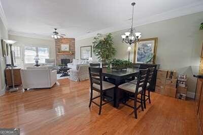 dining area with wood-type flooring, ceiling fan with notable chandelier, ornamental molding, and a large fireplace