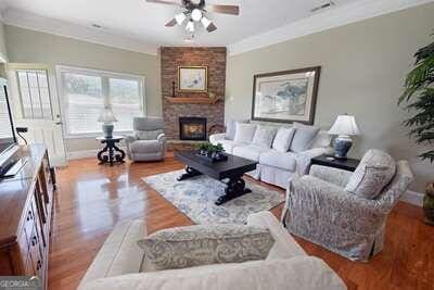 living room featuring ceiling fan, a stone fireplace, light hardwood / wood-style flooring, and crown molding