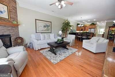 living room featuring ceiling fan with notable chandelier, hardwood / wood-style floors, and a stone fireplace