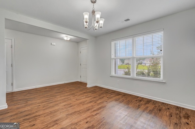 empty room with hardwood / wood-style floors and an inviting chandelier