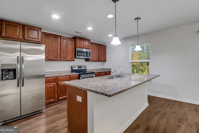 kitchen with dark hardwood / wood-style flooring, stainless steel appliances, sink, decorative light fixtures, and a center island with sink