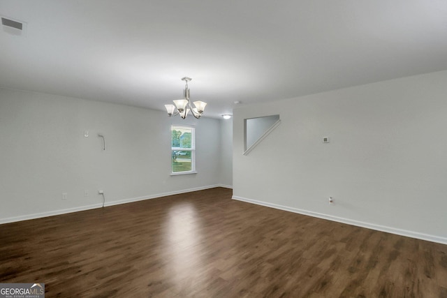 empty room with dark wood-type flooring and an inviting chandelier