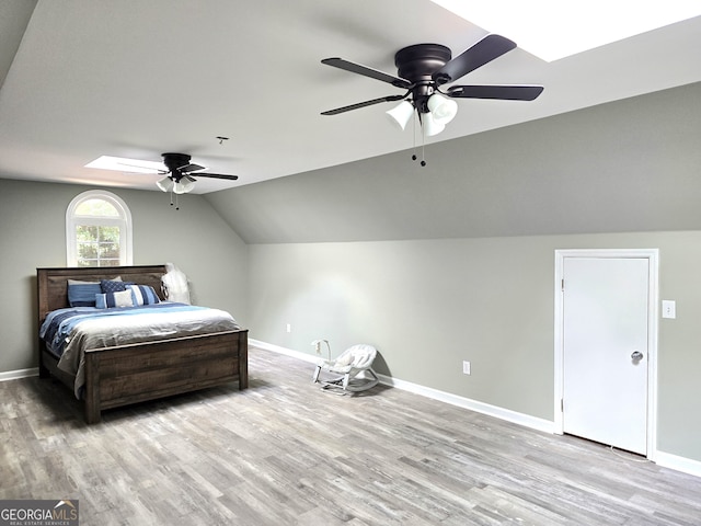 bedroom featuring lofted ceiling with skylight, ceiling fan, and light hardwood / wood-style flooring