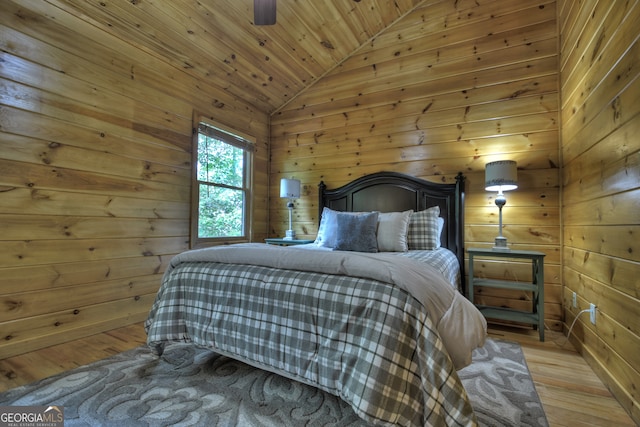 bedroom featuring light hardwood / wood-style flooring, wood walls, vaulted ceiling, and multiple windows