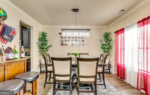 dining room featuring an inviting chandelier, ornamental molding, indoor bar, and dark hardwood / wood-style flooring