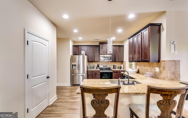 kitchen featuring kitchen peninsula, stainless steel appliances, sink, decorative light fixtures, and light hardwood / wood-style floors