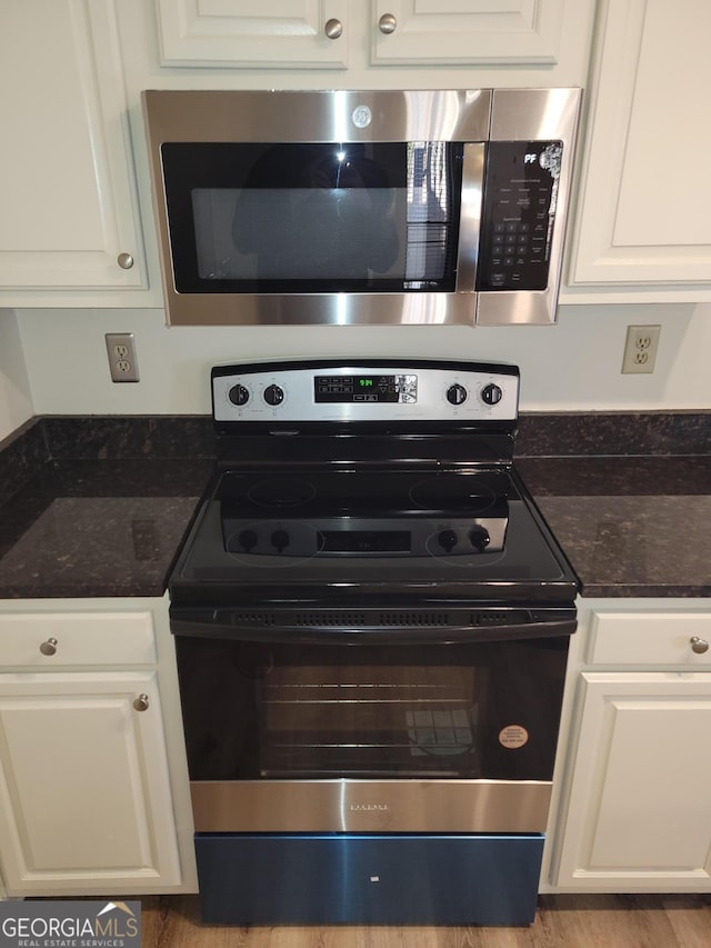 kitchen featuring appliances with stainless steel finishes, dark stone countertops, and white cabinetry