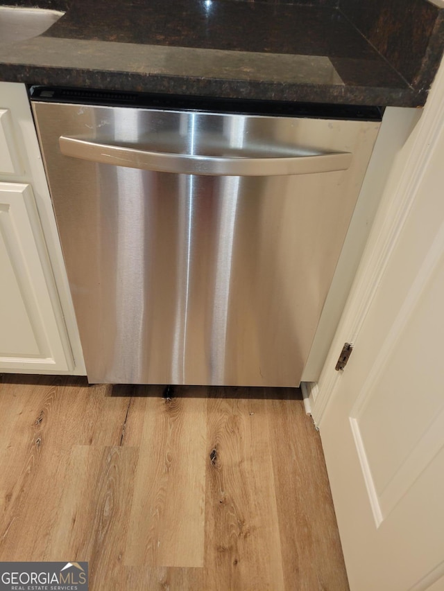 interior details featuring white cabinetry, stainless steel dishwasher, and dark stone counters