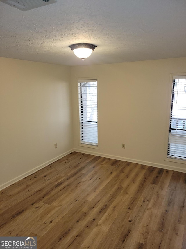 unfurnished room with a healthy amount of sunlight, a textured ceiling, and hardwood / wood-style floors