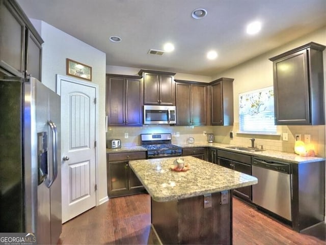 kitchen with a center island, dark wood-type flooring, sink, light stone countertops, and stainless steel appliances