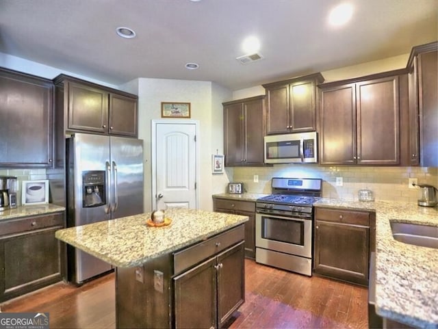 kitchen featuring dark hardwood / wood-style floors, tasteful backsplash, a kitchen island, light stone counters, and stainless steel appliances