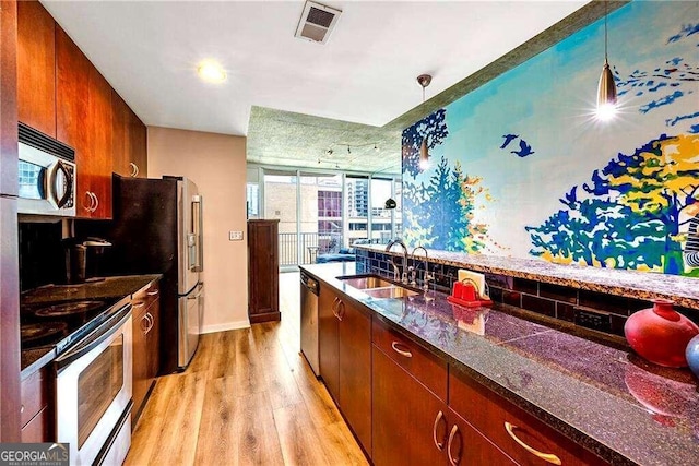 kitchen with decorative light fixtures, sink, appliances with stainless steel finishes, and light hardwood / wood-style floors