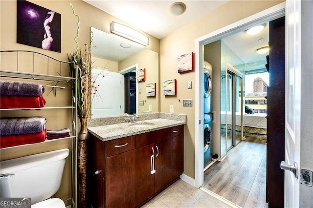 bathroom featuring wood-type flooring, stacked washing maching and dryer, vanity, and toilet