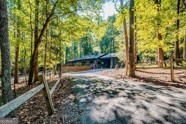 view of front of home featuring aphalt driveway, an attached garage, a view of trees, and fence