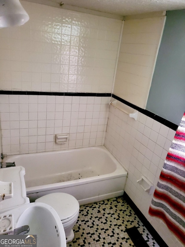 bathroom with a bath, tile walls, a textured ceiling, and toilet