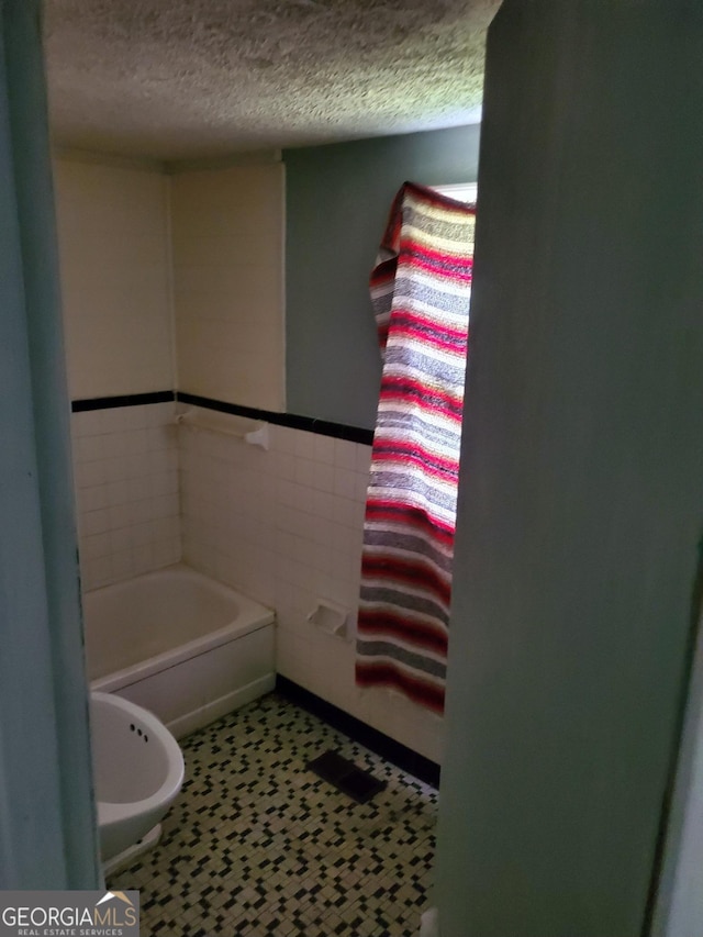 bathroom with a textured ceiling, a bathing tub, and tile walls