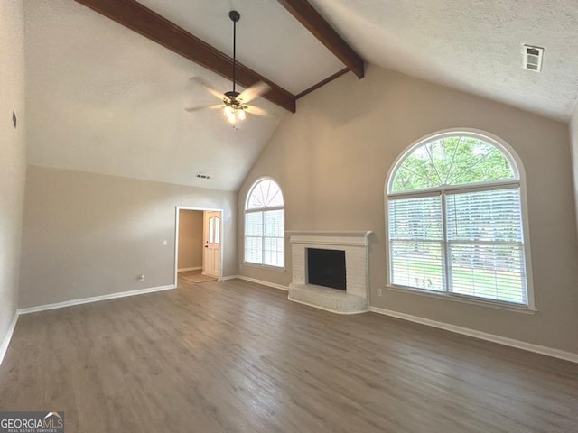 unfurnished living room with a brick fireplace, dark hardwood / wood-style flooring, a textured ceiling, beam ceiling, and ceiling fan