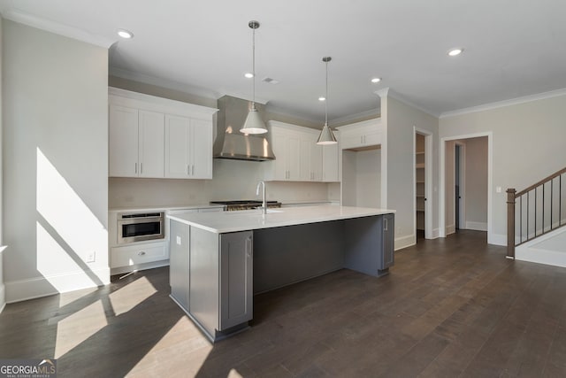 kitchen with a kitchen island with sink, white cabinets, wall chimney exhaust hood, dark hardwood / wood-style flooring, and stainless steel oven