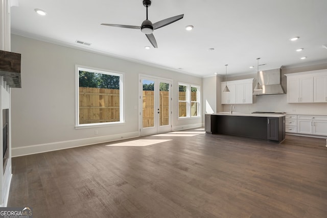 kitchen with ceiling fan, pendant lighting, a center island with sink, wall chimney exhaust hood, and white cabinetry