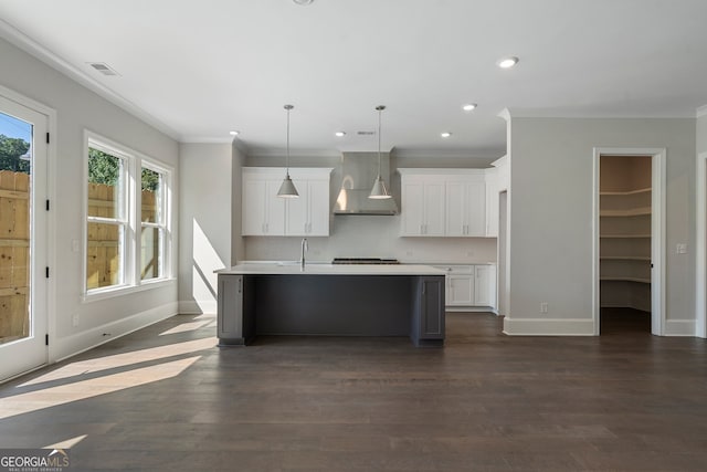 kitchen featuring dark wood-type flooring, white cabinets, decorative light fixtures, a center island with sink, and wall chimney range hood