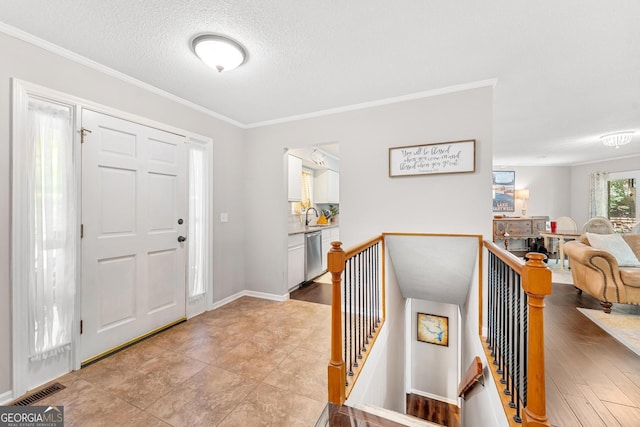 foyer with ornamental molding, light wood-type flooring, a textured ceiling, and sink