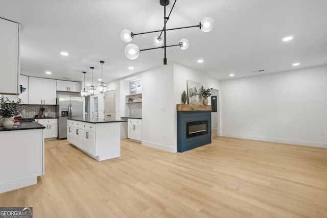 kitchen featuring hanging light fixtures, stainless steel fridge, white cabinetry, a center island, and light hardwood / wood-style flooring