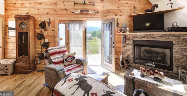 living room featuring light hardwood / wood-style flooring, wooden walls, vaulted ceiling, and a stone fireplace