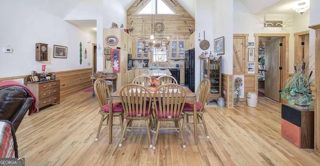 dining space featuring high vaulted ceiling, wooden walls, and light wood-type flooring