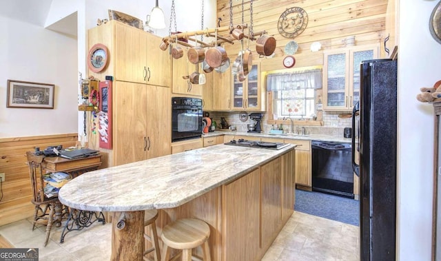 kitchen with wood walls, backsplash, black appliances, a breakfast bar, and light stone countertops